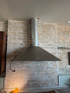 Kitchen range hood and duct vent installed against a brick wall